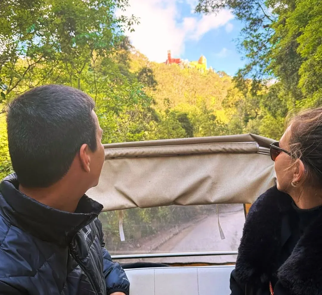 Gäste in einem Tuk-Tuk von YourTuk mit dem Pena-Palast im Hintergrund, in Sintra.