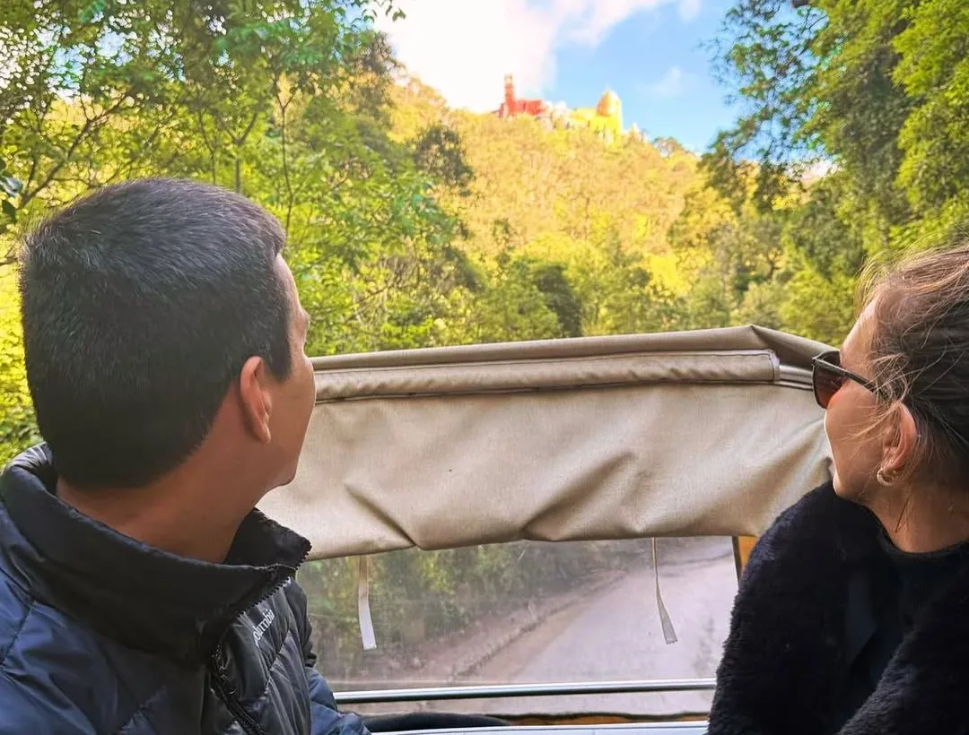 Guests in a YourTuk tuk-tuk with Pena Palace in the background, in Sintra.